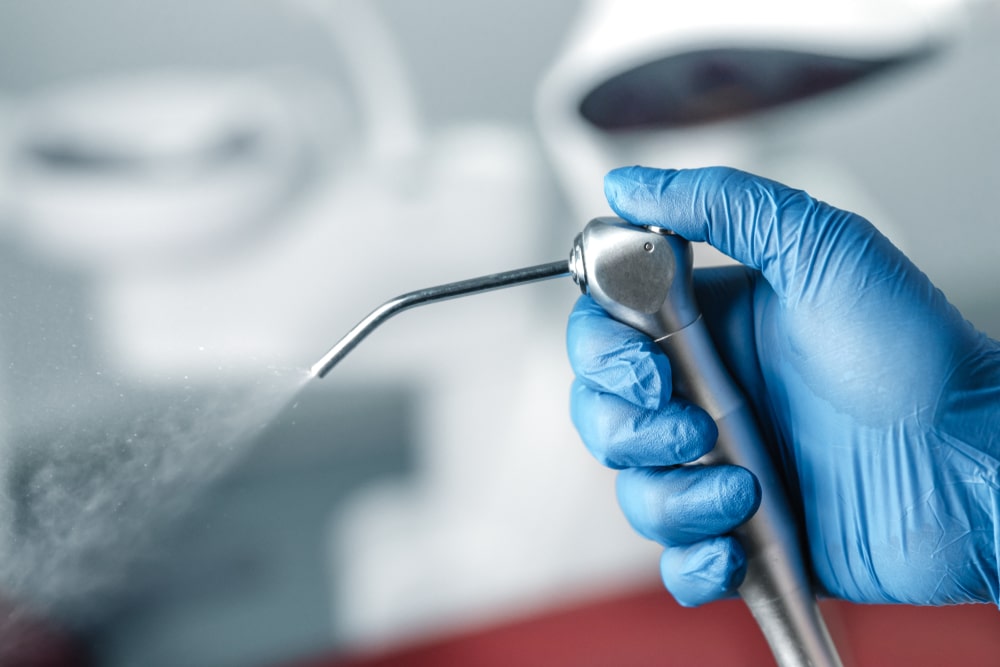 Female hand of dentist in blue gloves holding air water syringe,